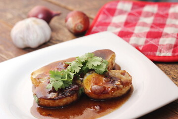 Egg with Tamarind Sauce in a white plate served on a wooden table with coriander sprinkles, is a popular local dish that Thai people eat.