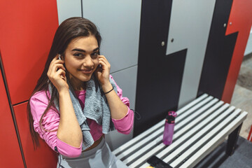 Cropped shot of an attractive young female listening to music while sitting in the dressing room. Fitness woman taking a break after running workout.