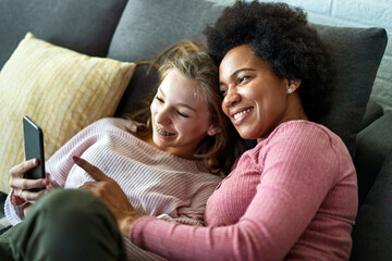 Happy african american mother and teen daughter using smartphone apps for shopping social media