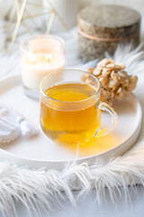 Cup of herbal tea and burning candle on round white decorative tray
