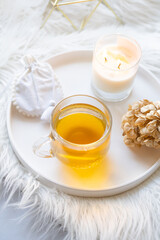 Cup of herbal tea and burning candle on round white decorative tray