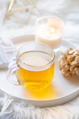 Cup of herbal tea and burning candle on round white decorative tray