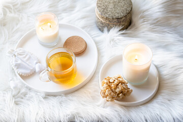 Cup of herbal tea and burning candle on round white decorative tray