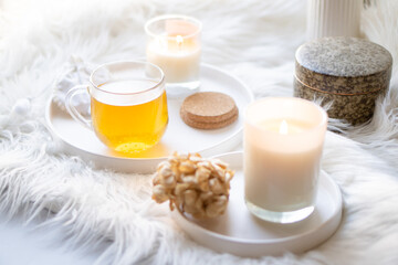 Cup of herbal tea and burning candle on round white decorative tray