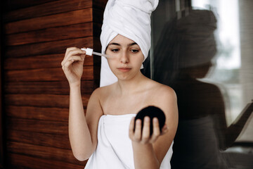 Young girl with towel on her head makes facial treatments. Skin care, moisturizing with serum