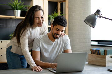Happy interracial couple smiling while working or having fun at laptop