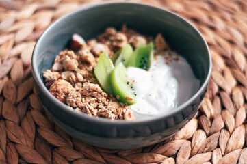 Roasted healthy homemade granola with Gluten Free Rolled oats or porridge oats, variety of chopped nuts and seeds and fresh kiwi pieces. Portion of granola and kefir or yogurt in bowl