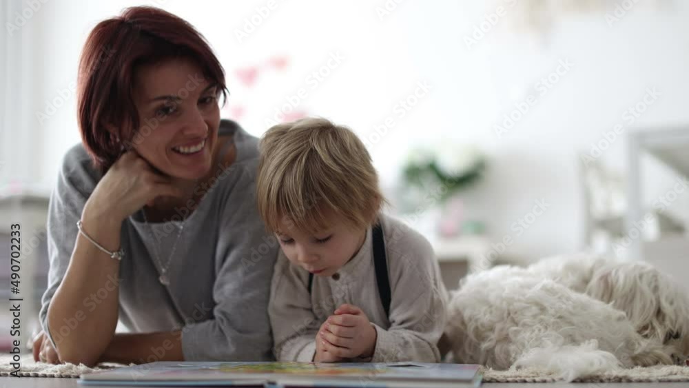 Sticker Cute blond preschool child, blond boy with pet maltese dog, reading book at home on the floor with mother