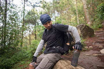 Hiking man relaxing and drinking water from bottle after trekking in the mountains
