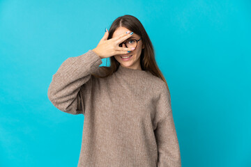 Young Lithuanian woman isolated on blue background covering eyes by hands and smiling
