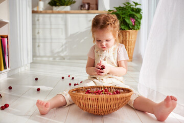 cute toddler baby girl playing with cherries, sitting on the floor in sunny room