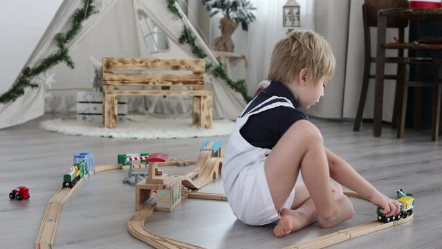 Cute blond toddler child, boy, playing with colorful trains and railroad at home on the floor