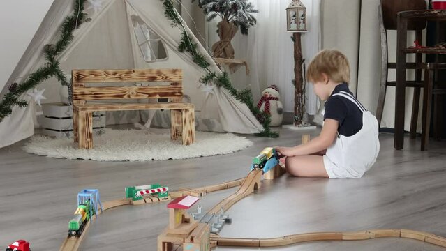 Cute blond toddler child, boy, playing with colorful trains and railroad at home on the floor