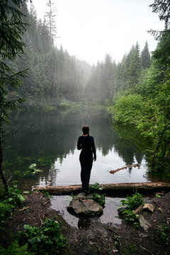 Beautiful ukrainian nature. Woman standing hean forest lake surrounded with pine trees. Carpathian Mountains, Rosohan, Ukraine