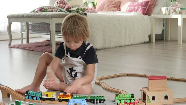 Cute blond toddler child, boy, playing with colorful trains and railroad at home on the floor