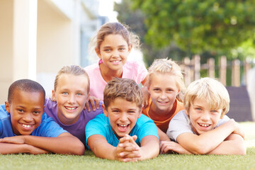 We love having fun together after school. Group portrait of happy school kids lying in a pile outside in the sun.