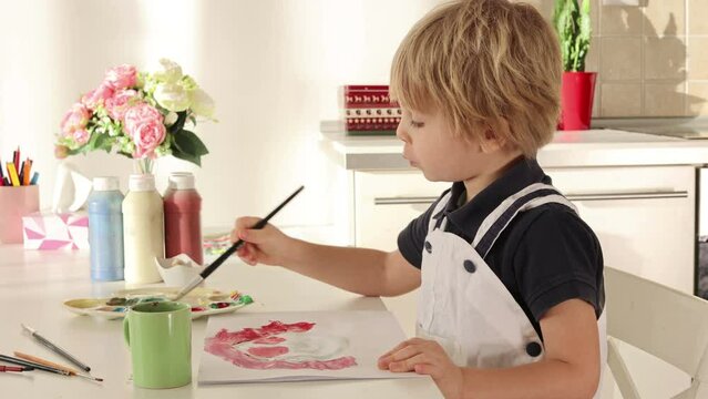 Cute blond boy, preschool child, painting at home with aquarelle colors card for Valentine