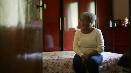 One senior black woman sitting by bedside in bedroom - Powered by Adobe