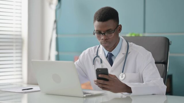Young African Doctor using Smartphone while using Laptop in Office 