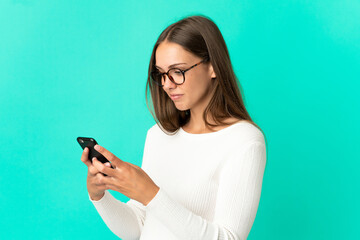 Young woman over isolated blue background sending a message or email with the mobile