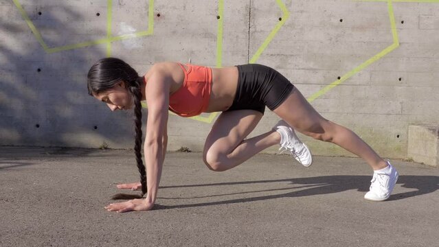 Fit athletic woman doing plank knee raises outdoors 