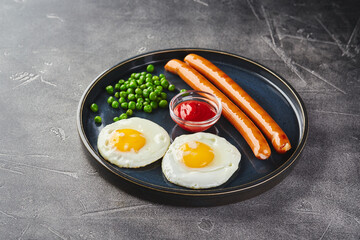 Classic breakfast of fried eggs, sausages and green peas on dish on gray background