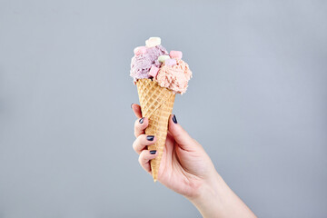 Two scoops of ice cream in waffle cone in female hand on gray background