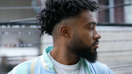 A pensive black man standing in drizzle thinking profile of young person