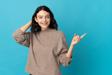 Teenager Ukrainian girl isolated on blue background surprised and pointing finger to the side