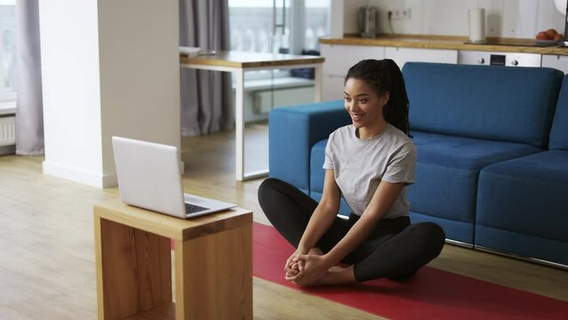 Young African woman doing stretching, warming up her joints in front laptop