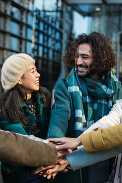 Cheerful diverse coworkers stacking hands together with colleagues on city street
