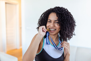 Portrait of playful young female runner smiling aside and biting her gold medal . Sports, active lifestyle, motivation concept - obrazy, fototapety, plakaty