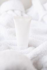 Clean white cosmetic cream tube on fluffy white cotton towel background, mock-up and design ready