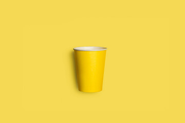 Vaso de papel reutilizable amarillo sobre un fondo amarillo liso y aislado. Vista superior y de...