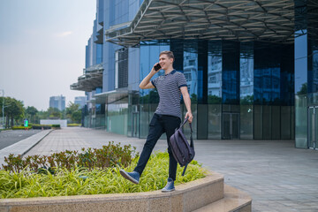 Young caucasian man walking near modern office buildings and making phone call