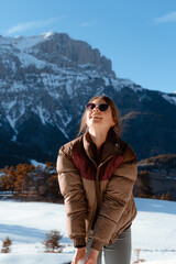 Fototapeta na wymiar Pretty happy woman with sunglasses and warm jacket in snowy winter mountain landscape