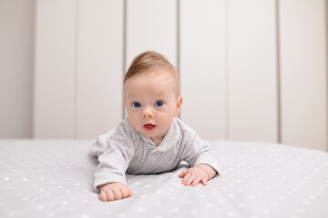 Child care Concept. Portrait of cute little baby wearing bodysuit lying on white bed sheets at home. Black infant child crawling on bed in the bedroom. Selective focus, free copy space