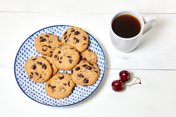 White cup with coffee, traditional cookies and sweet cherries on a white wooden background, closeup. Tasty breakfast, morning routine concept