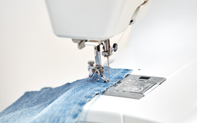 Sewing machine working part with blue denim cloth, replacement foot. A close-up shows a needle passing through tissue. Sewing machine with fabric and thread