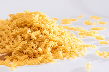 Uncooked Fusilli Pasta Scattered on Wooden Board and White Table. Raw and Dry Macaroni. Fat and...