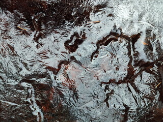 Thin ice texture on dark water of a stream.