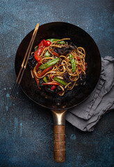 Asian dish stir fry udon noodles with vegetables and mushrooms in black rustic wok pan with wooden...
