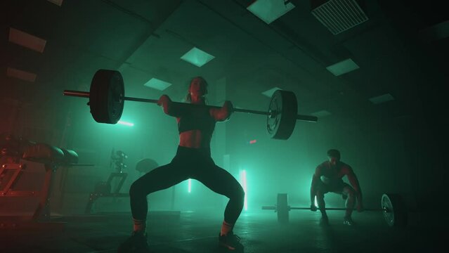 powerlifting training in fitness hall, two person are lifting barbells in dark hall, physical exercise