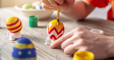 A woman's hand with a brush is drawing a colored pattern on an Easter egg. Preparation for the bright Easter holiday