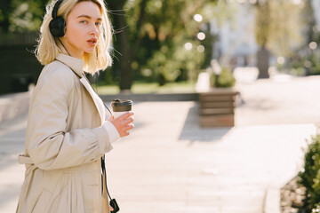 Blonde walks in summer city with cup of coffee