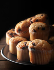 Close up or macro photography, vanilla cupcakes with chocolate chips on a white plate over a wooden table in front of a window. concept of homemade sweet bread