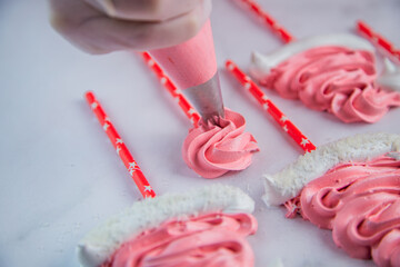 From the pastry bag, the pastry chef squeezes out a zigzag meringue on white parchment and a red...