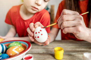 Woman's hand with a brush is drawing a colored pattern on an Easter egg. Creative preparation for bright Easter holiday