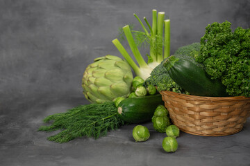 Green vegetables and herbs assortment on a grey stone background. Copy space.