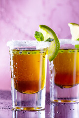 two brown shot cocktails garnished with lime and salt. Shots on the bar, water drops and mint. Purple background